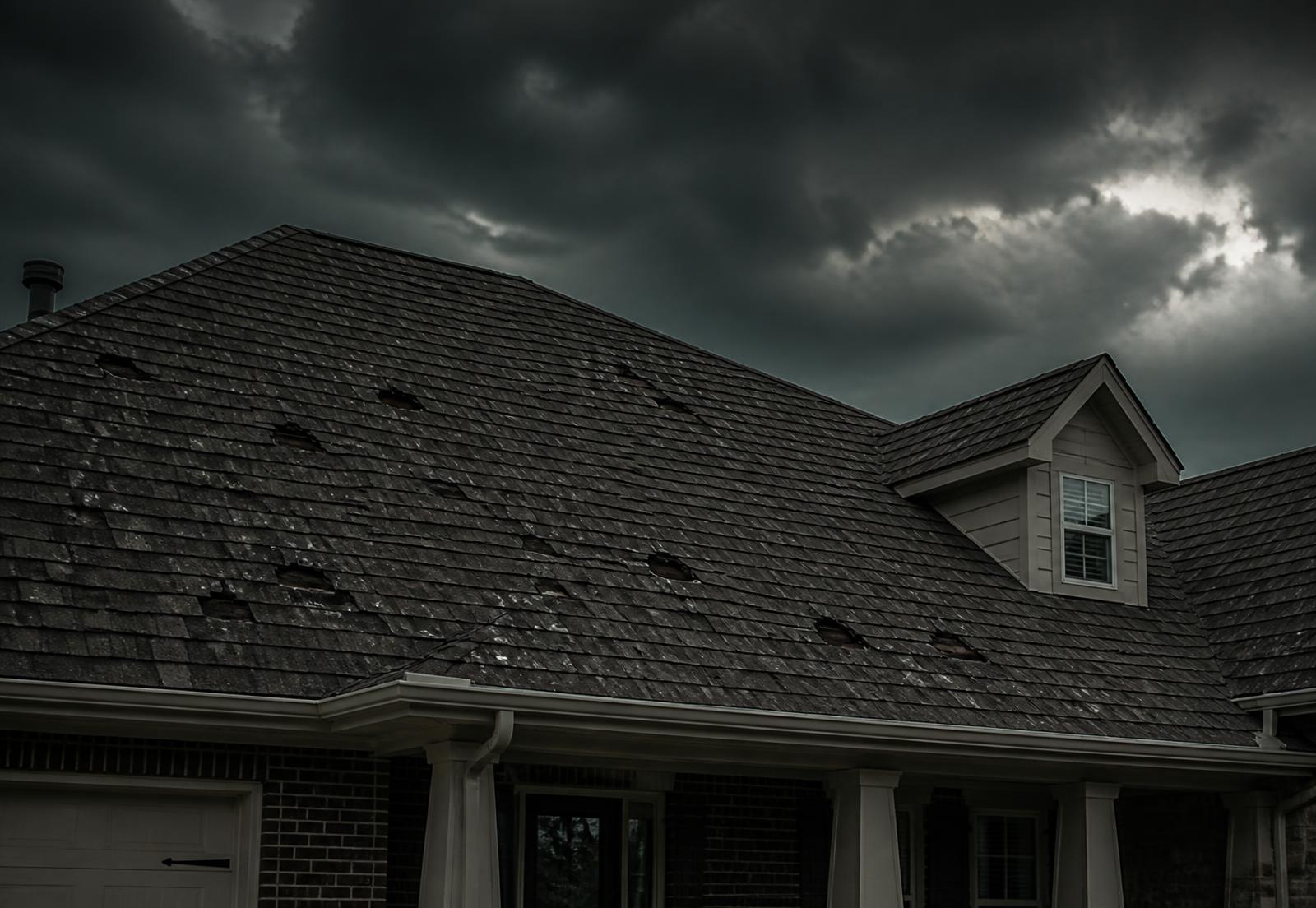 Hail-damaged asphalt shingle roof under a dark storm sky